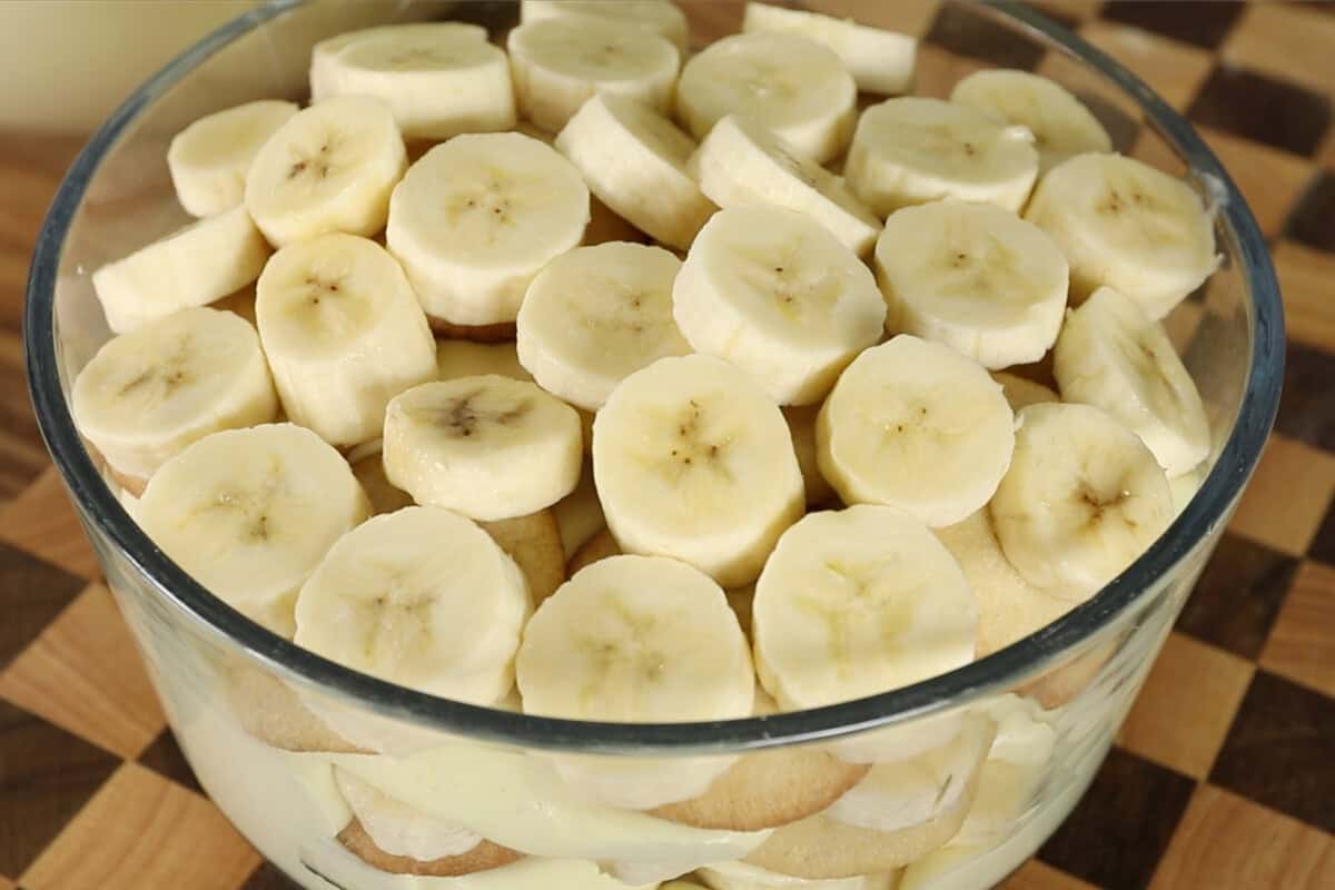 assembling vegan banana pudding with whipped cream in clear trifle dish