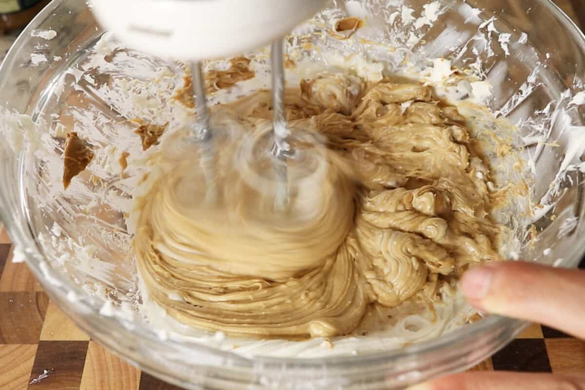 beating cookie butter and filling ingredients with a hand mixer in a large glass bowl