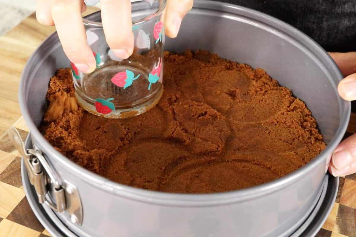 using a cup to press down cookie crust in a springform pan