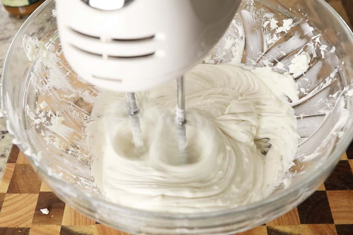 whipping cream cheese and sugar with a hand mixer in a large glass bowl