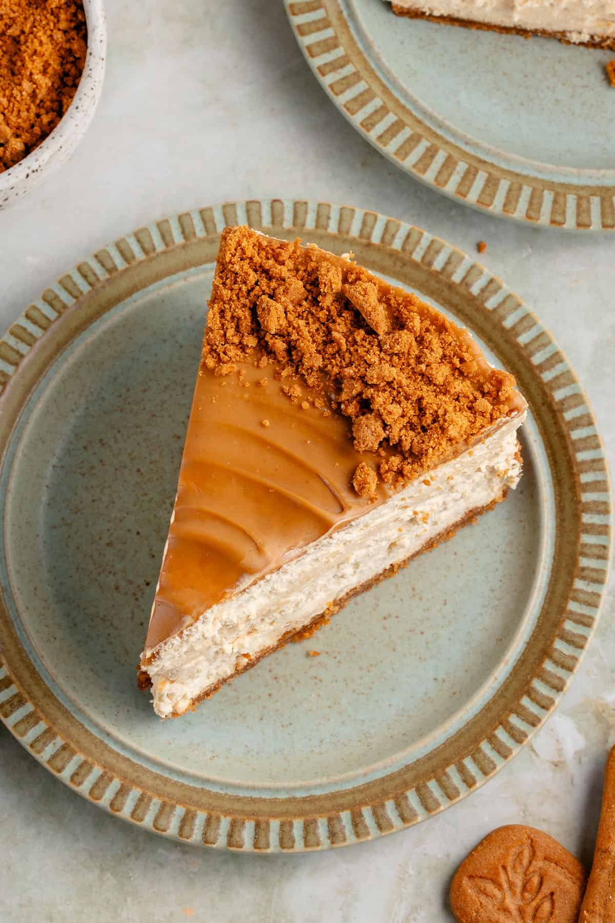 overhead image of vegan biscoff cheesecake on a blue plate with cookies and crumbs surrounding it