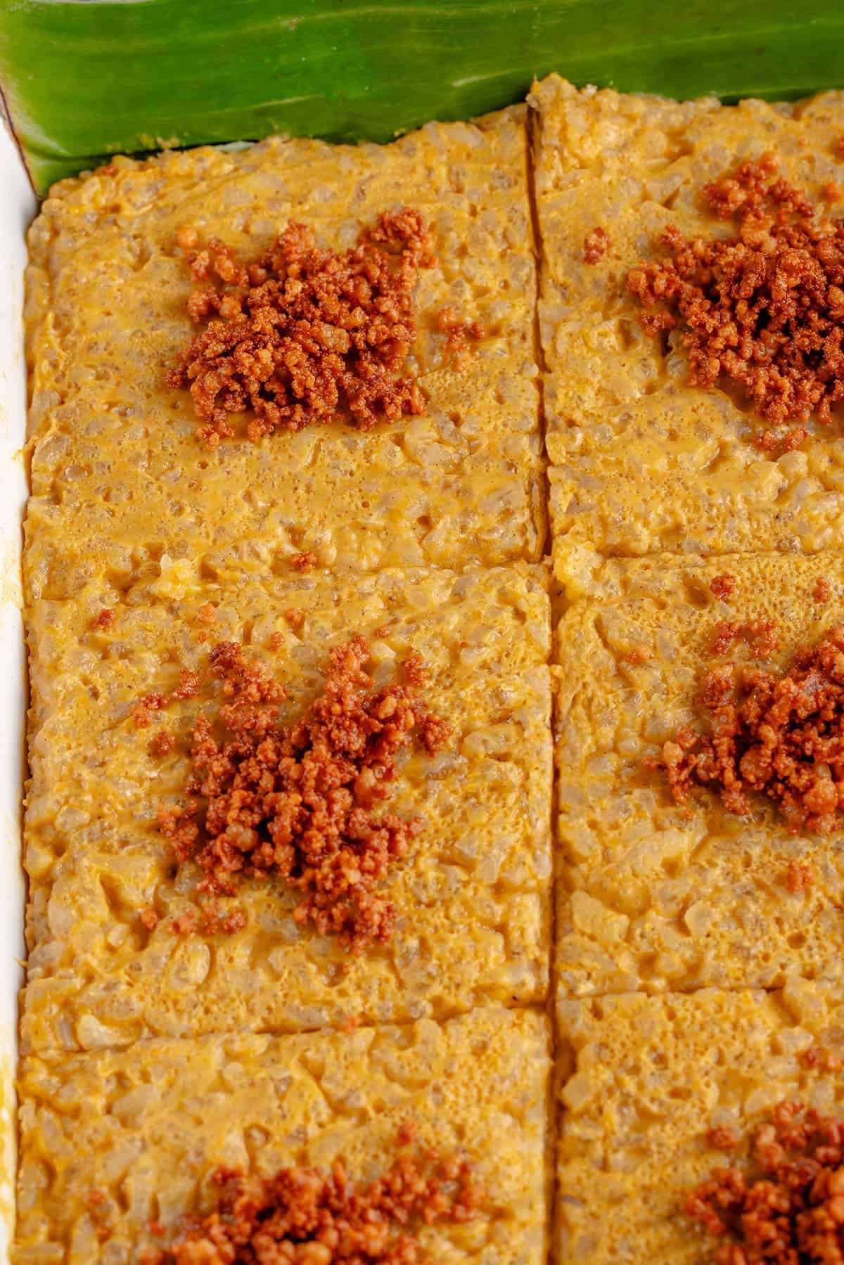 overhead photo of Biko Kalabasa (Pumpkin Biko) in a square baking dish with latik and banana leaves