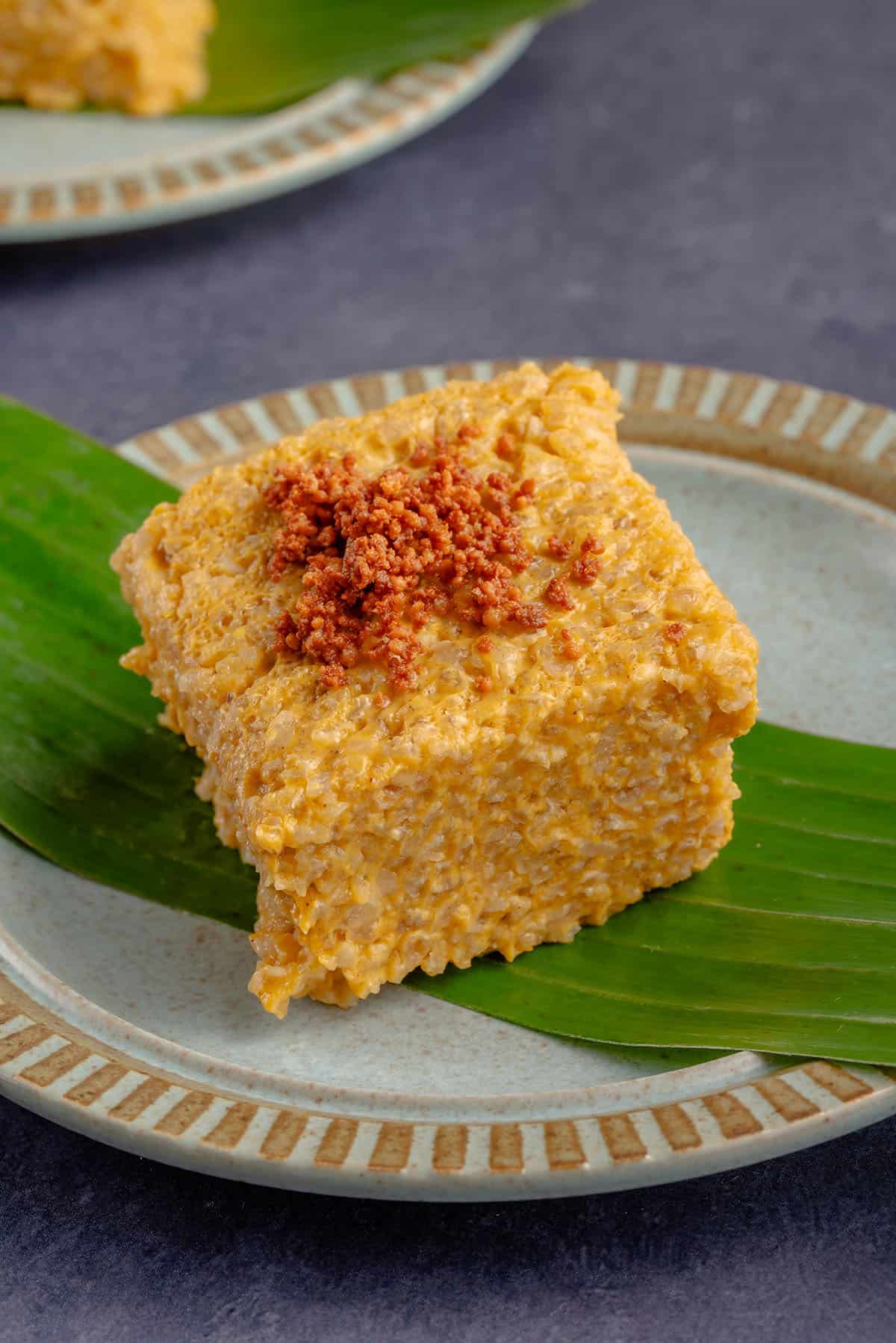 square piece of pumpkin biko with latik on a blue plate with a banana leaf and