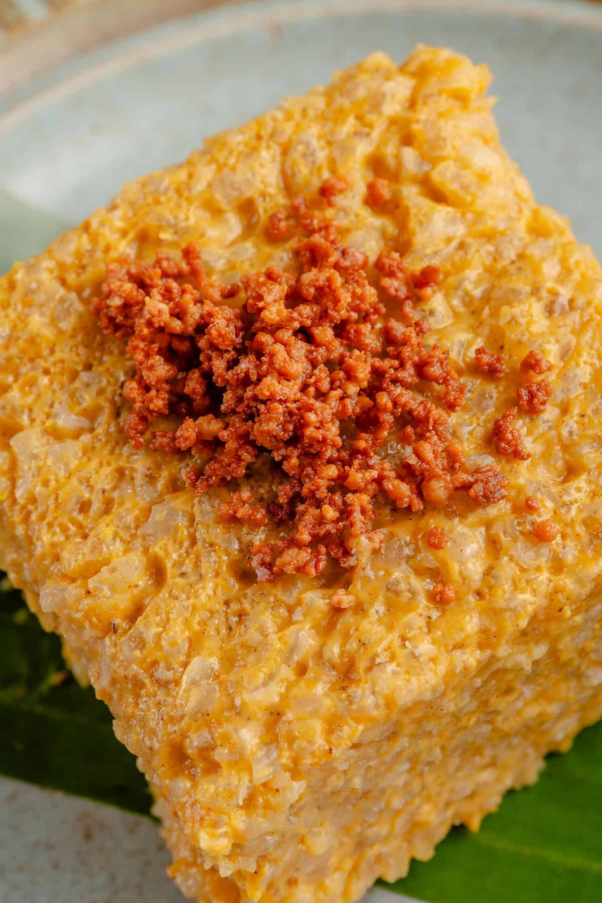 close up of a square piece of pumpkin biko with latik on a blue plate with a banana leaf and