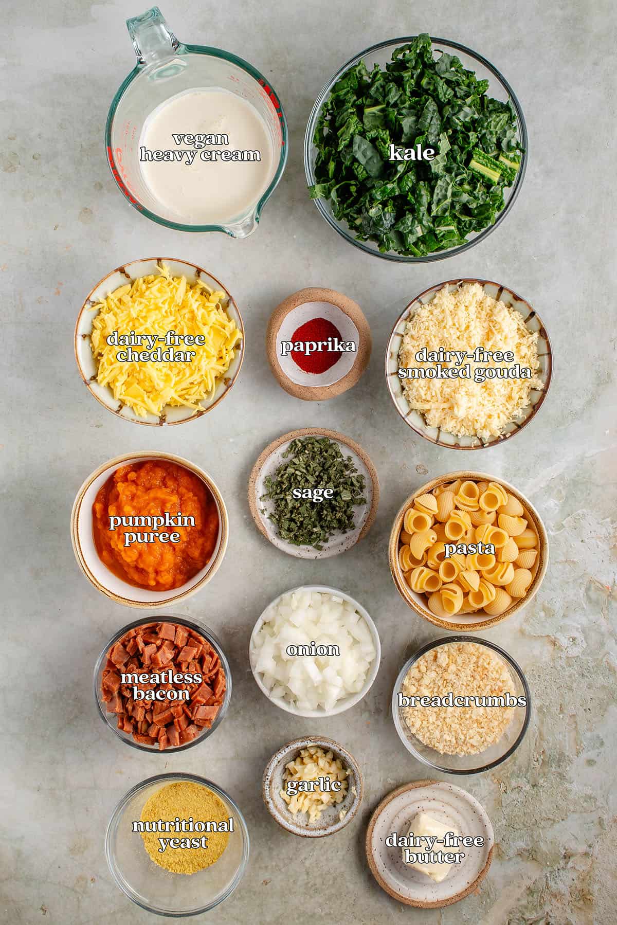 labeled ingredients for pumpkin mac and cheese: dairy-free butter, garlic, sage, breadcrumbs, dairy-free heavy cream, dairy-free smoked gouda, dairy-free cheddar, nutritional yeast, pasta, onion, garlic, kale, Meatless bacon, pumpkin purée and smoked paprika