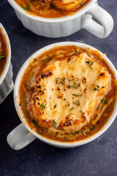 close up overhead photo of 3 bowls of french onion soup topped with toasted bread and melted vegan cheese with fresh thyme