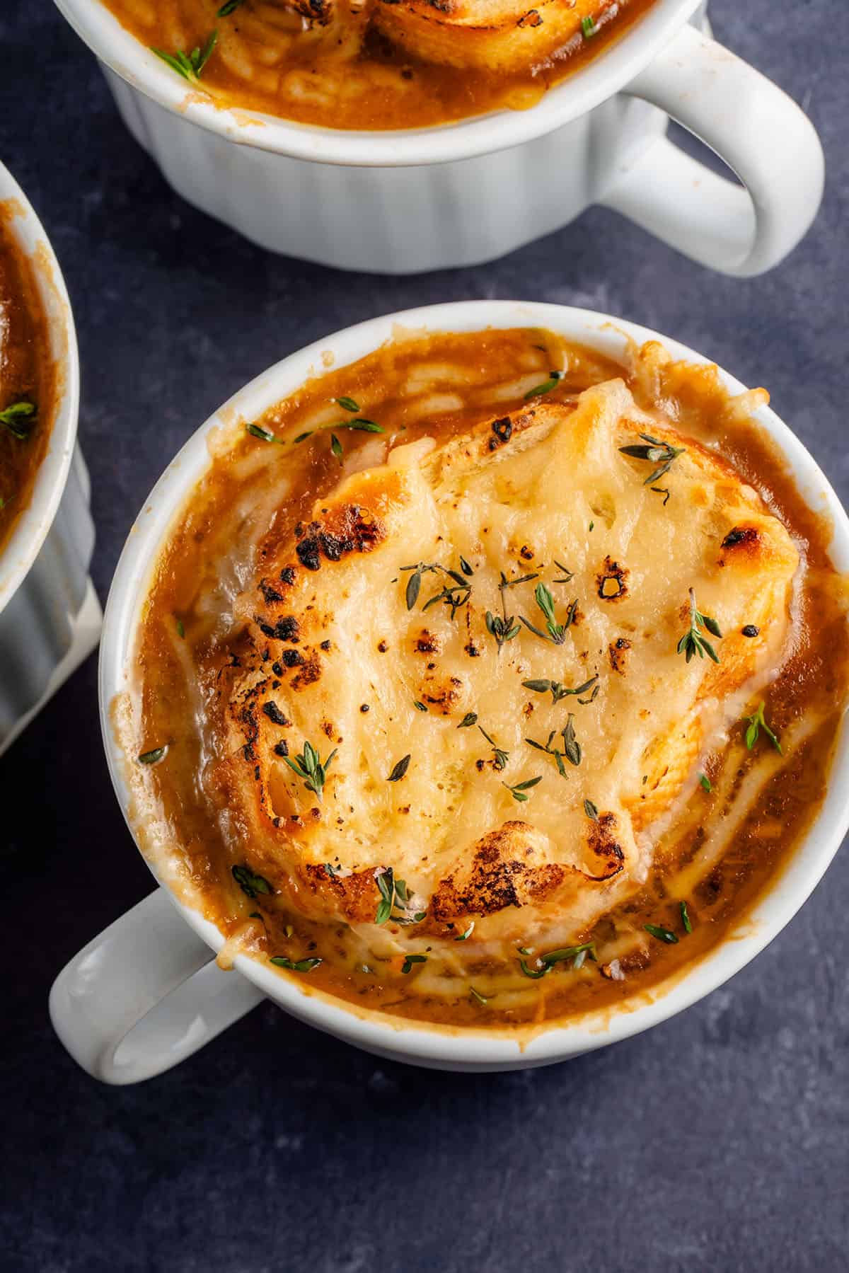 close up overhead photo of 3 bowls of french onion soup topped with toasted bread and melted vegan cheese with fresh thyme