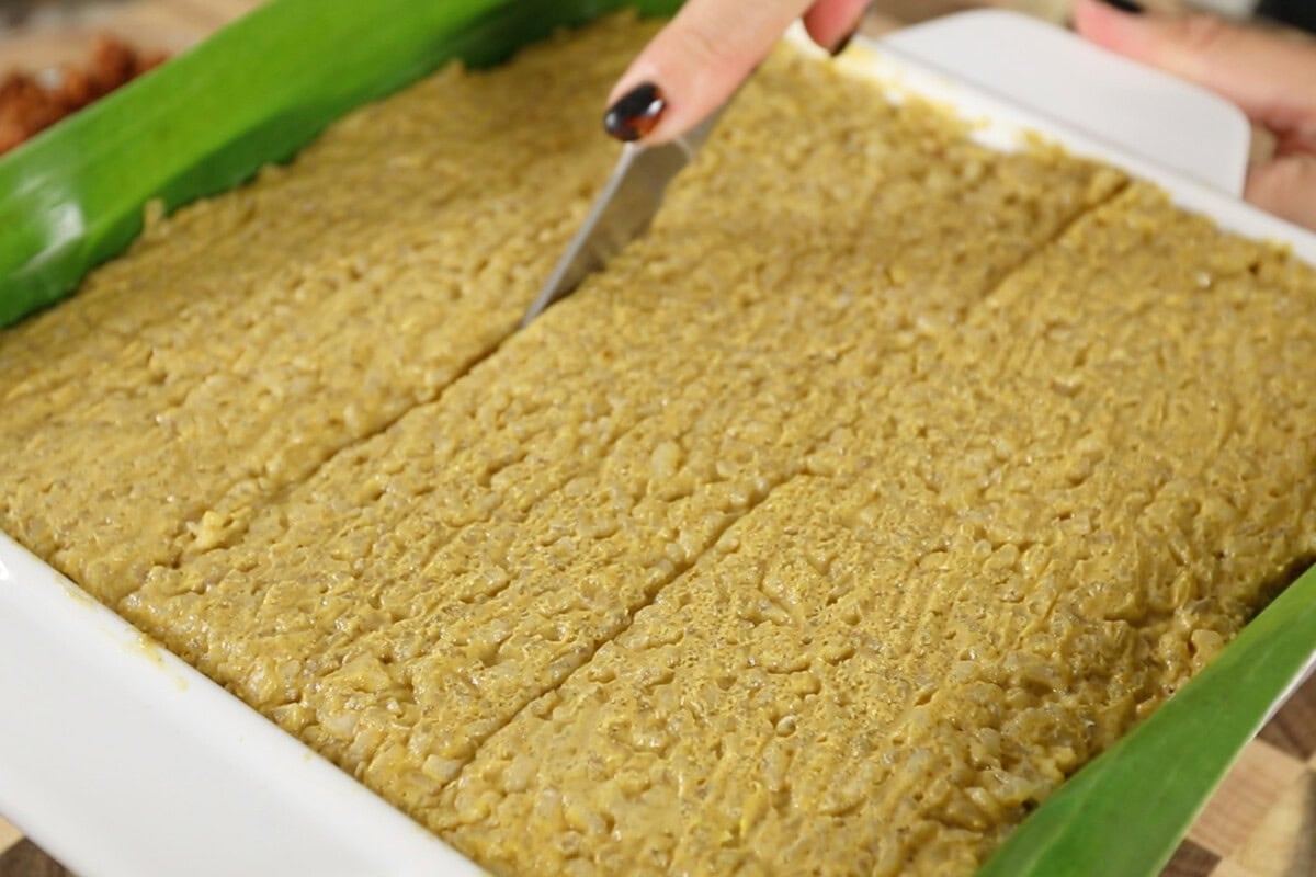 slicing Biko Kalabasa (Pumpkin Biko) in pan lined with banana leaves