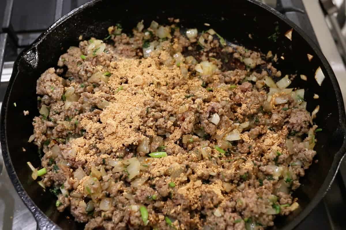 adding taco seasoning to the ground beef in a skillet