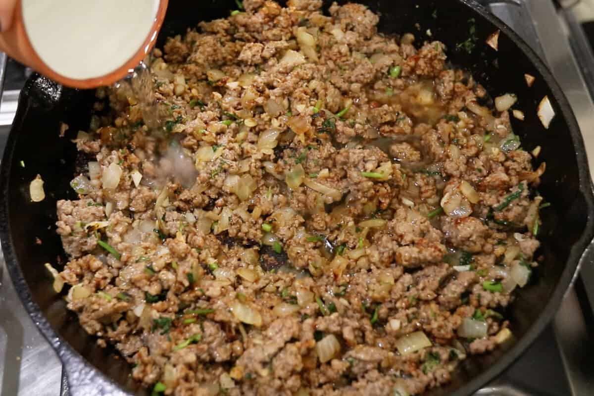 adding tequila to the ground beef in a skillet