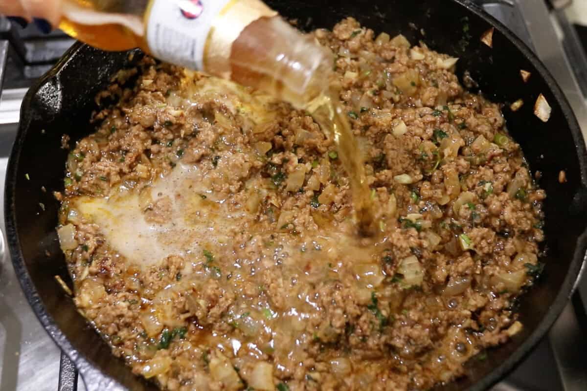 adding beer to the skillet of cooked ground beef