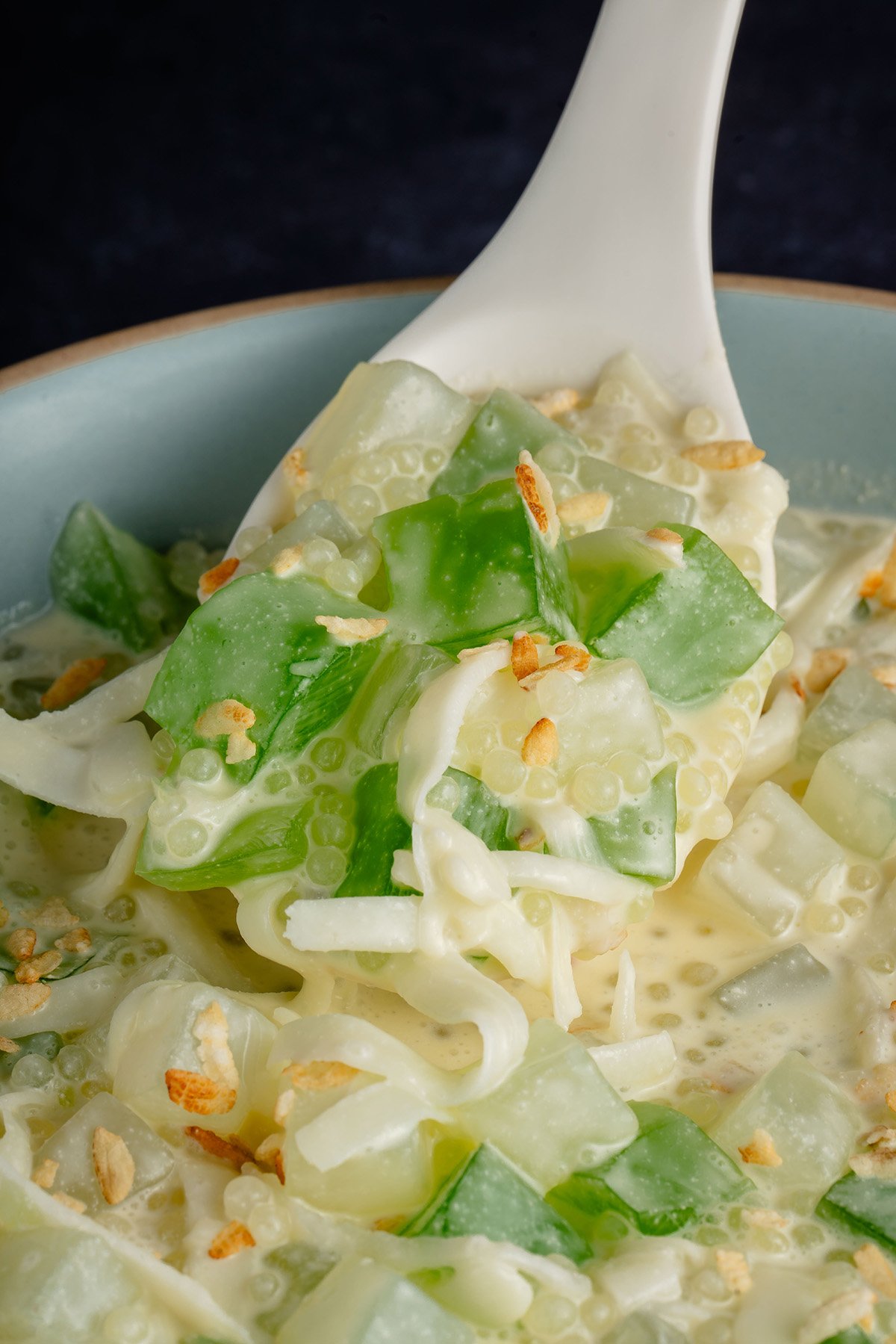 white spoon scooping Filipino Buko Pandan Salad out of blue bowl