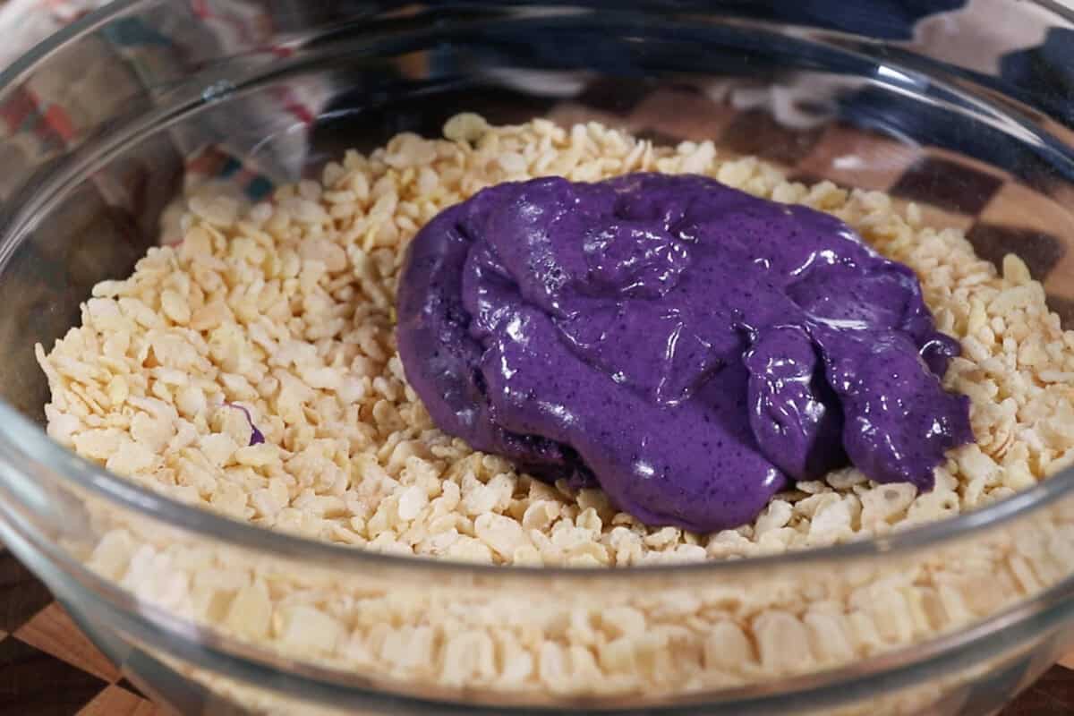 adding the ube marshmallow mixture to a large bowl of crispy rice cereal