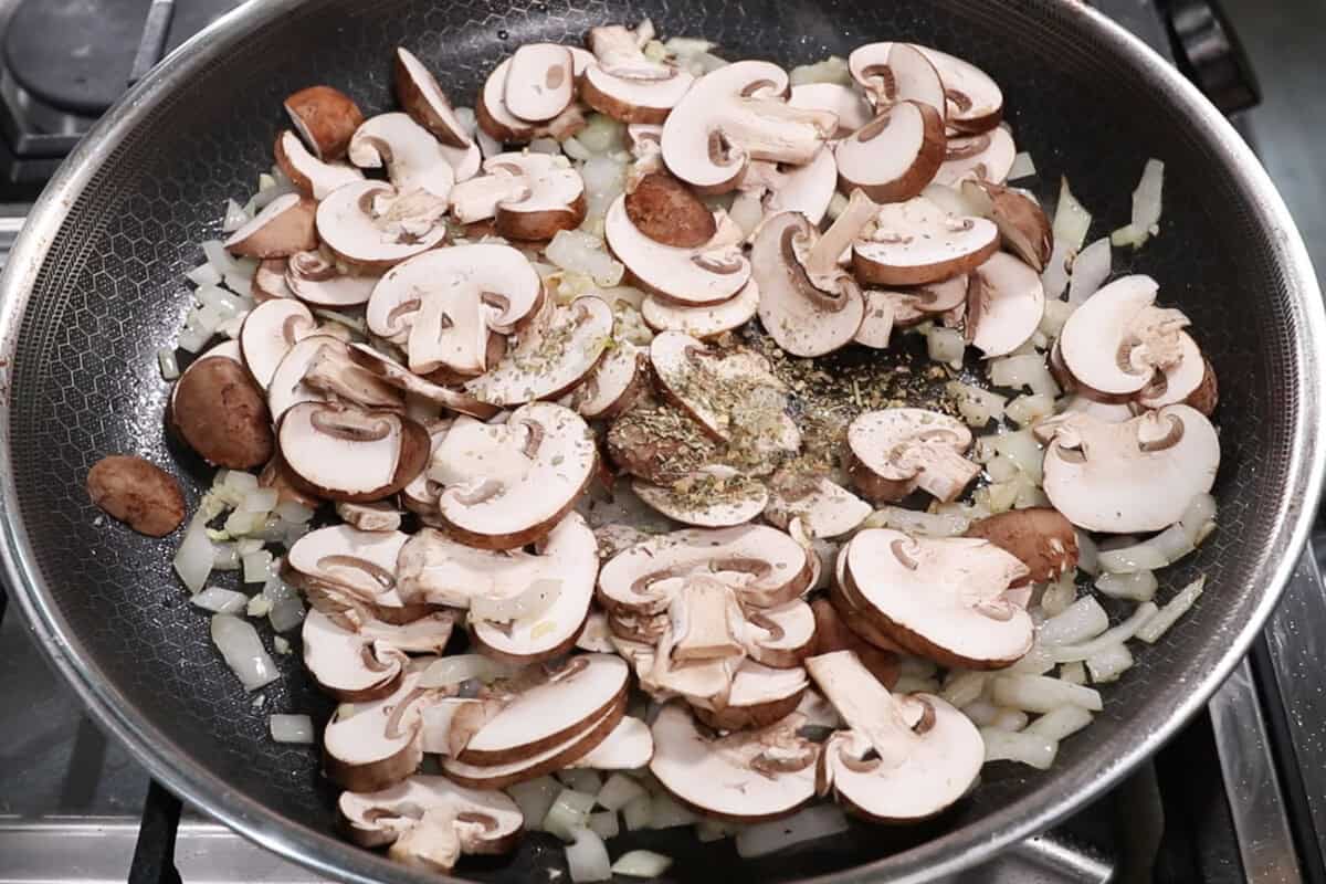 onions, mushrooms, and italian seasoning being sautéd in a large skillet