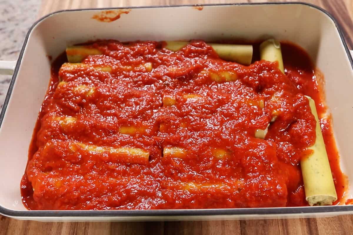 marinara sauce poured over top filled manicotti noodles