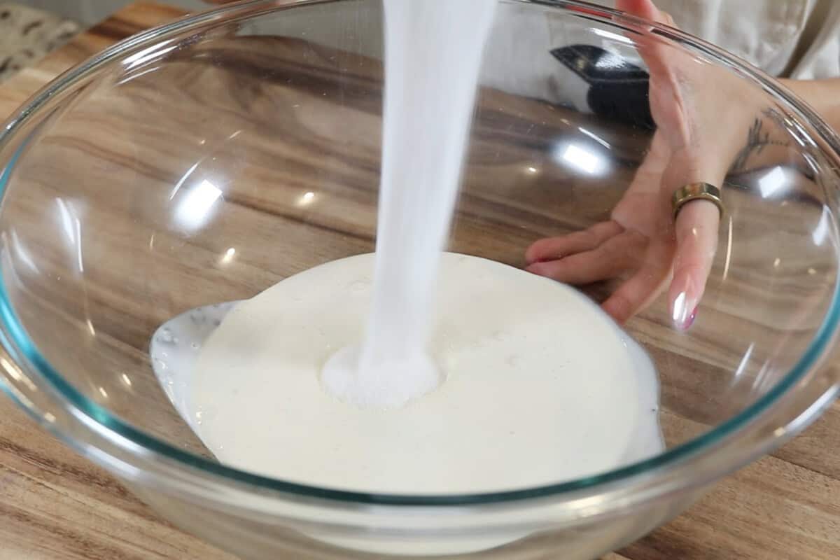 adding sugar to the large bowl of heavy cream