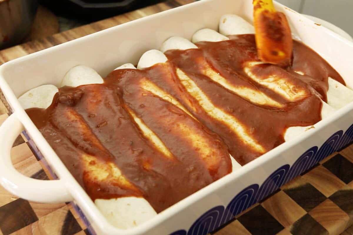 adding enchilada sauce over the rolled tortillas in a baking dish