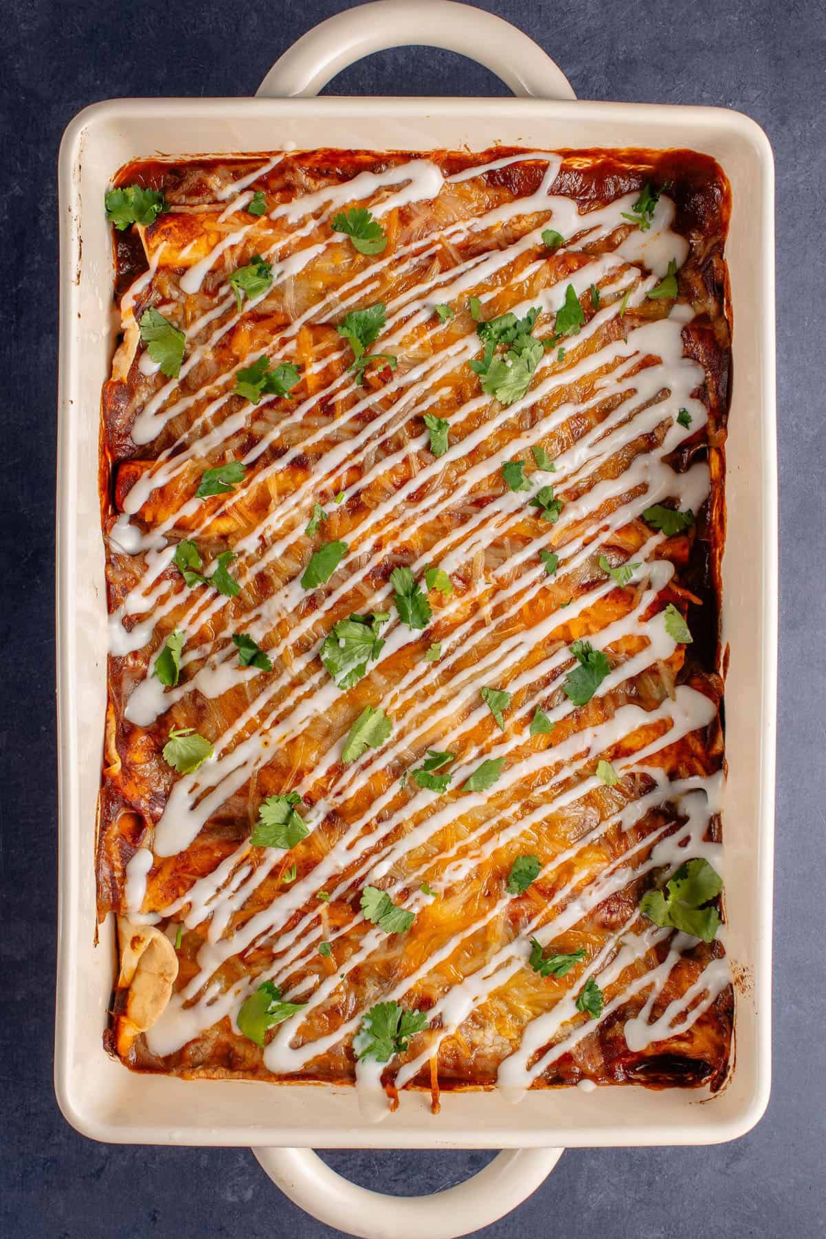 overhead of vegan enchiladas in baking dish topped with sour cream and cilantro