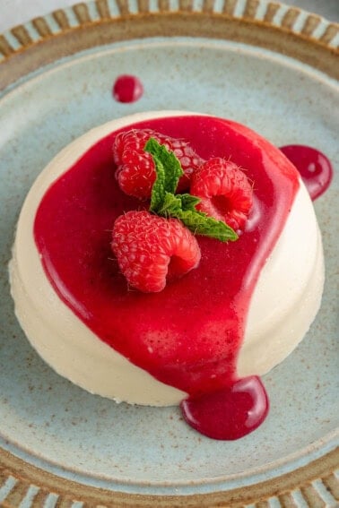 horizontal photo of vegan panna cotta on a blue plate with berry coulis with raspberries and mint