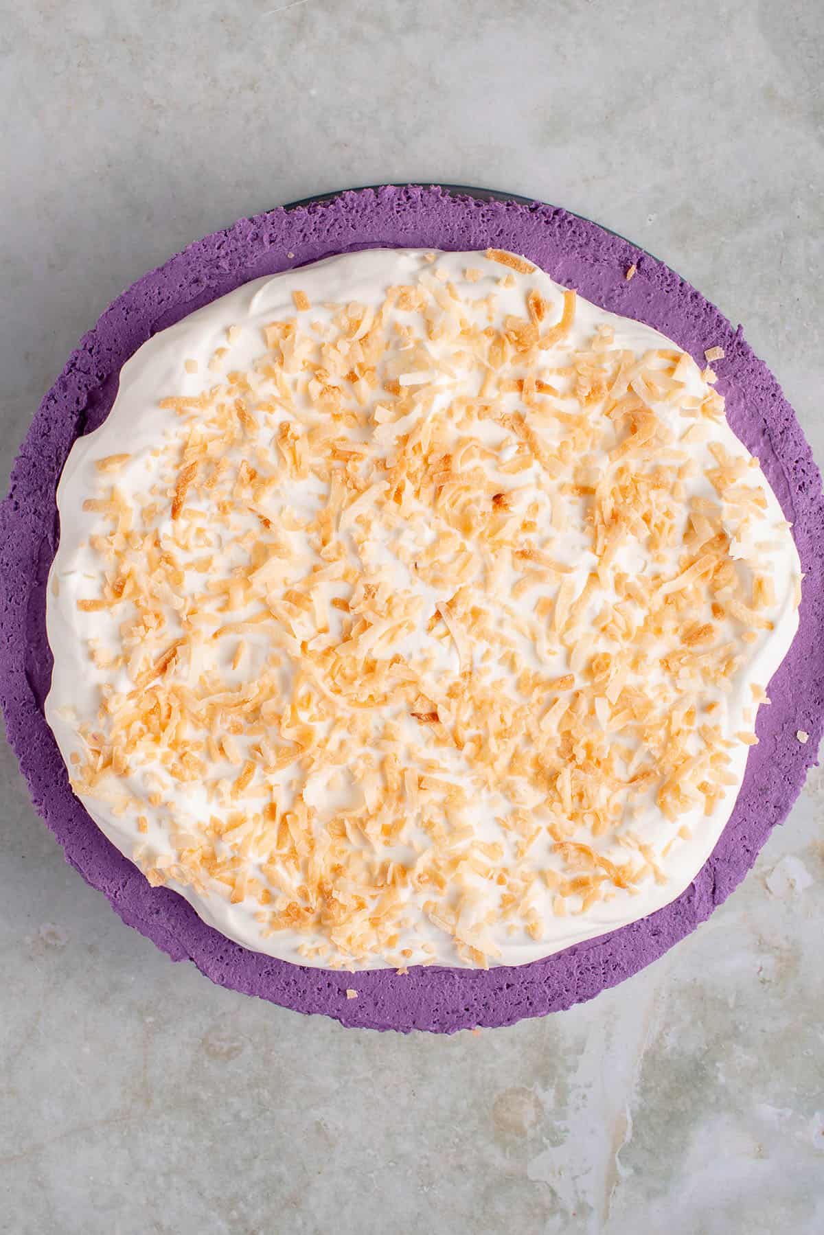 overhead of full ube cheesecake topped with whipped cream and toasted coconut flakes