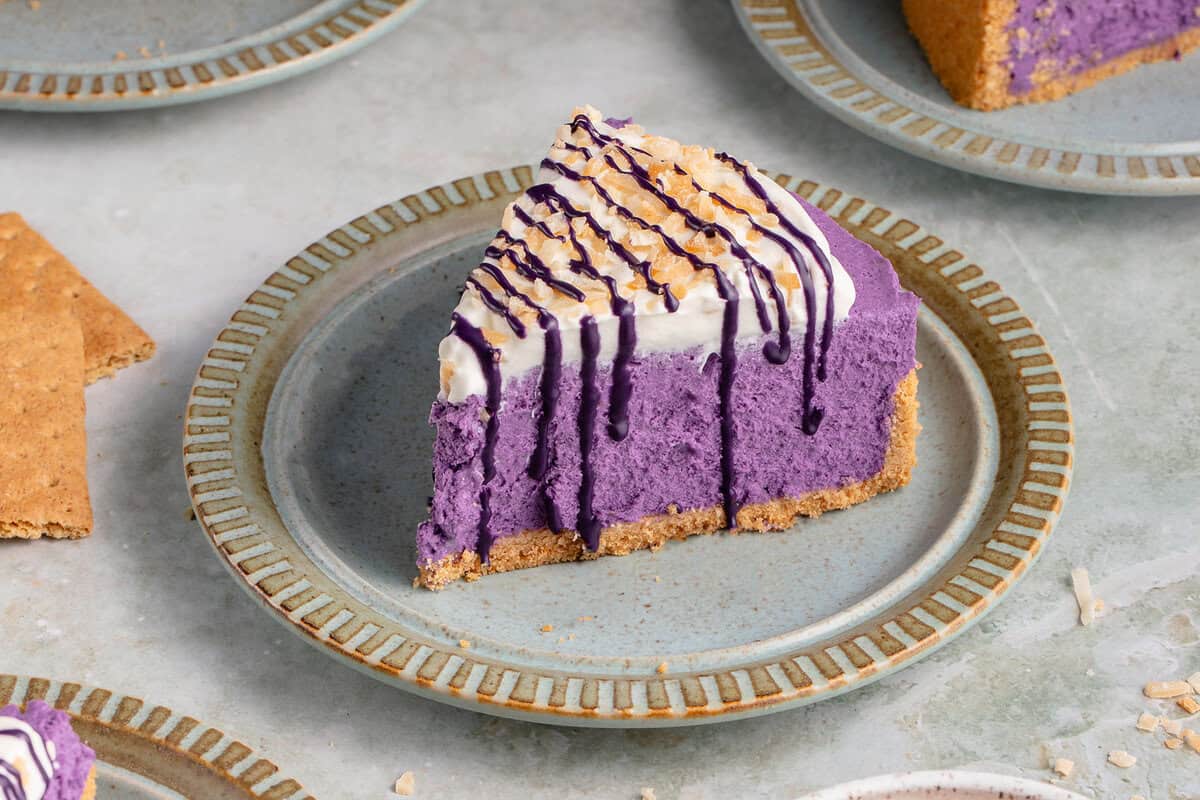 ube cheesecake on a blue plate surrounded by coconut flakes and graham crackers