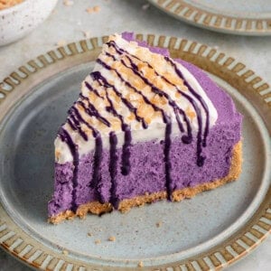 ube cheesecake on a blue plate surrounded by coconut flakes and graham crackers