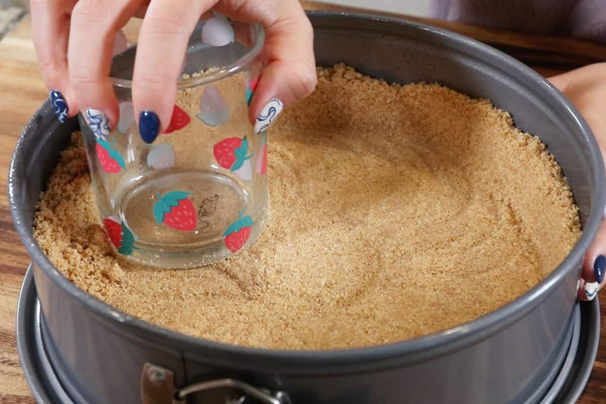 pressing down graham cracker crust with a glass