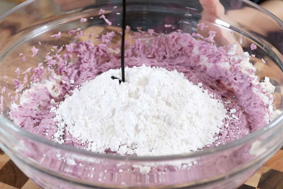 adding powdered sugar and ube extract to a bowl