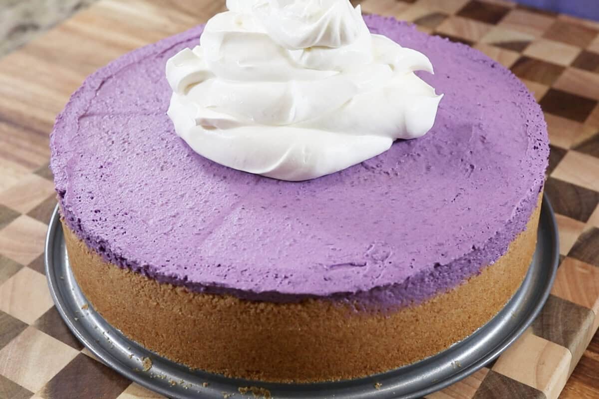 adding whipped cream to ube cheesecake