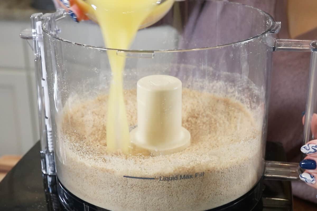 adding butter to powdered graham crackers in a food processor