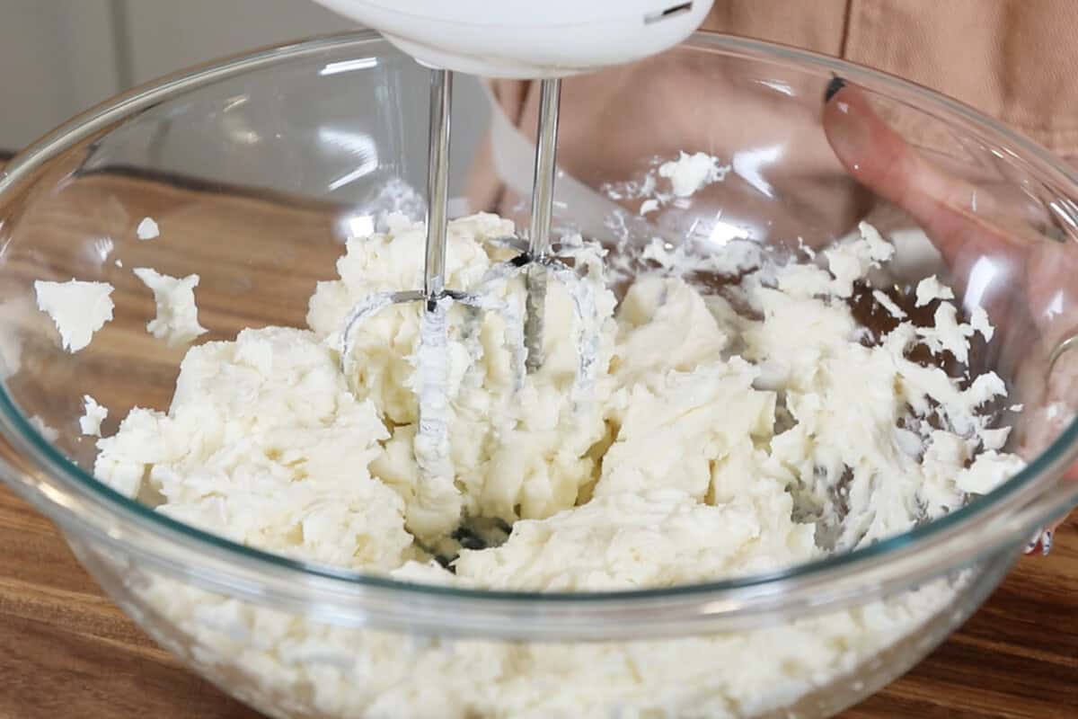 whipping vegan cream cheese and sugar in large glass bowl