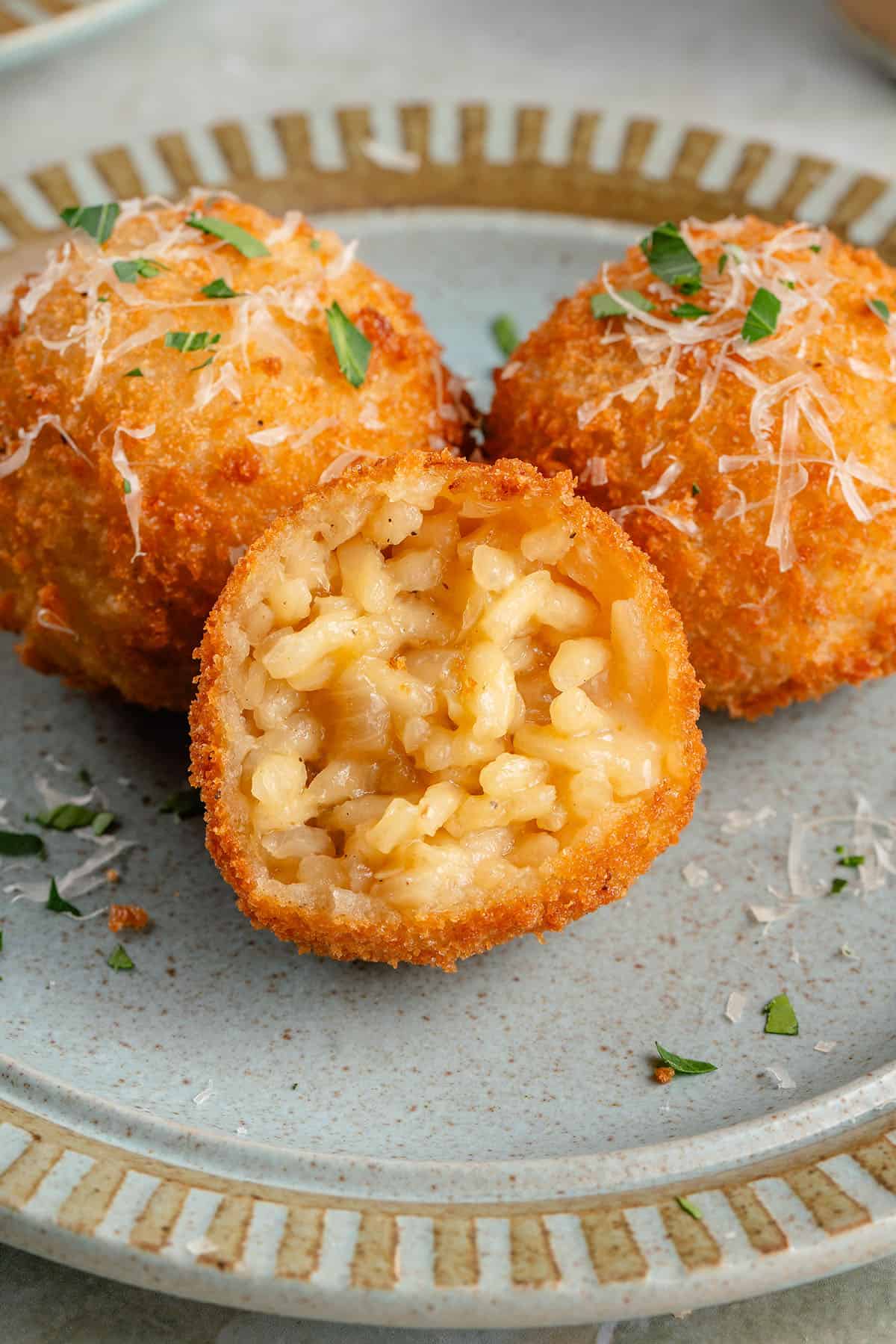 arancini with the inisde showing on blue plate topped with parmesan and fresh parsley