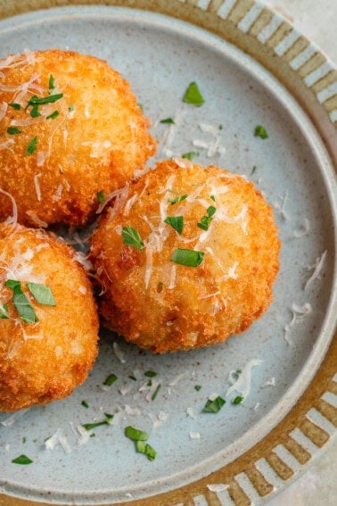 arancini on blue plate topped with parmesan and fresh parsley