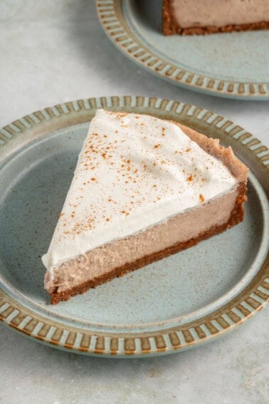 a slice of vegan chai spiced cheesecake with whipped cream and cinnamon on blue plate