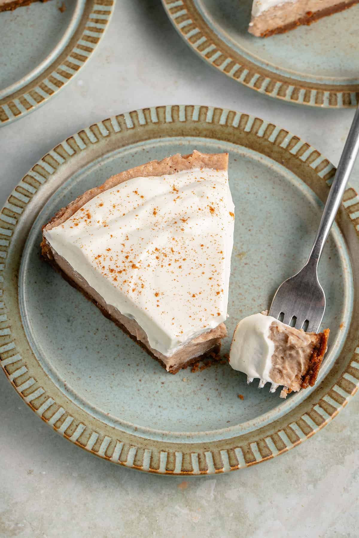 fork cut into a slice of vegan chai spiced cheesecake with whipped cream and cinnamon on blue plate