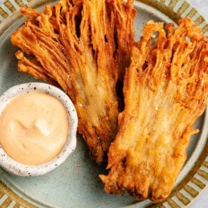 fried enoki mushrooms on a plate with a dipping sauce