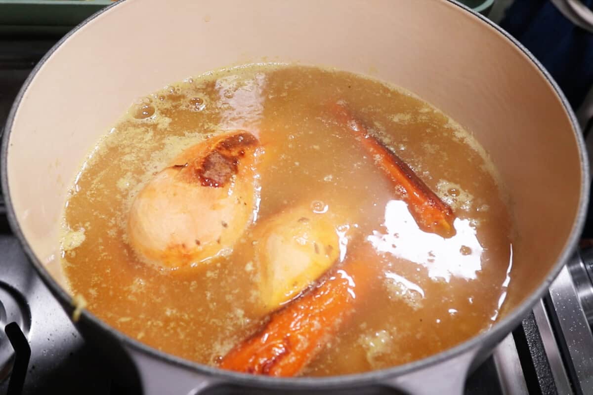 adding roasted veggies to a large pot of soup