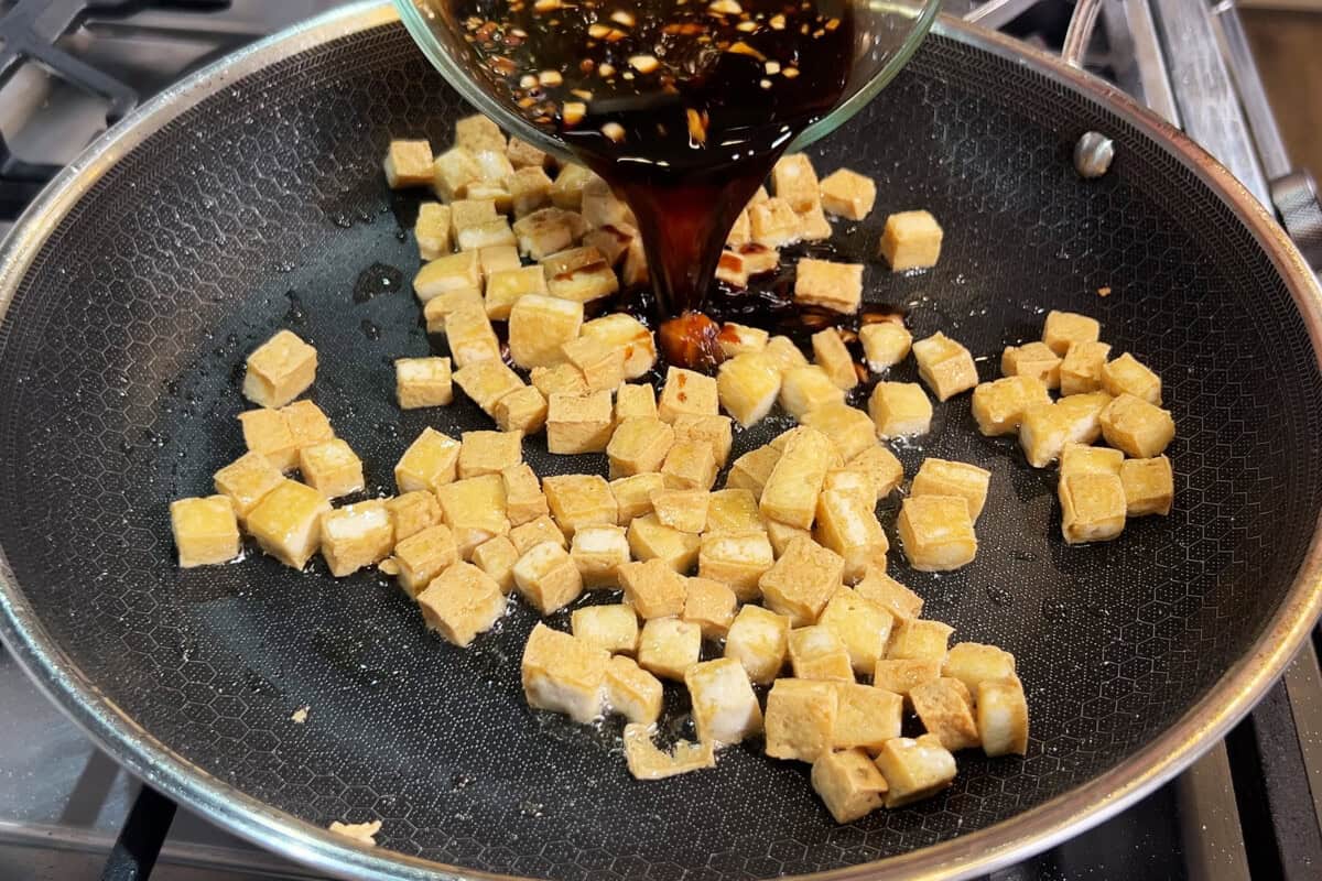 pouring sauce over tofu in skillet