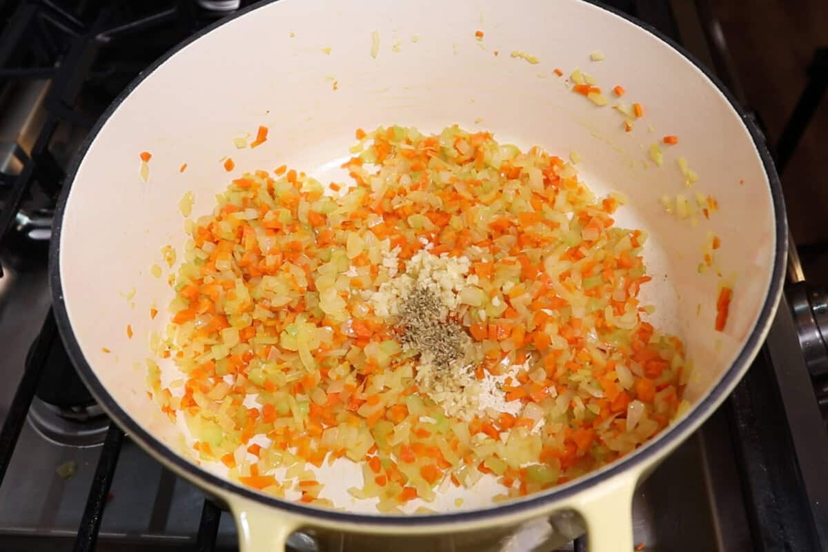 cooked celery, carrots, and onions in a pot with garlic and herbs just being added