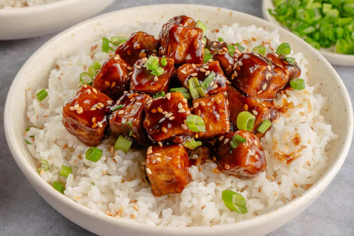 bowl of sticky sesame tofu with rice topped with green onions