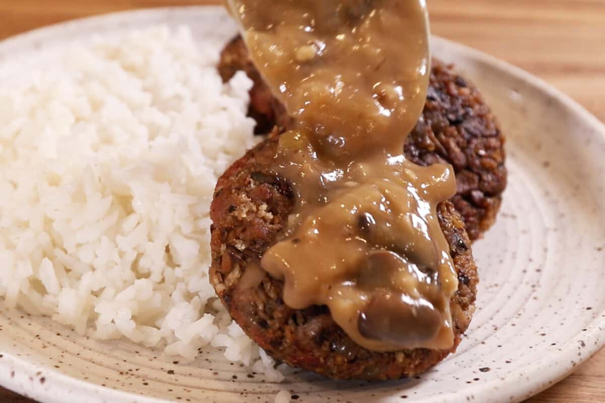 adding gravy to burger steak on plate with rice