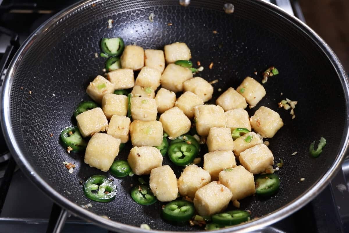 adding tofu and sliced jalapeños to the wok