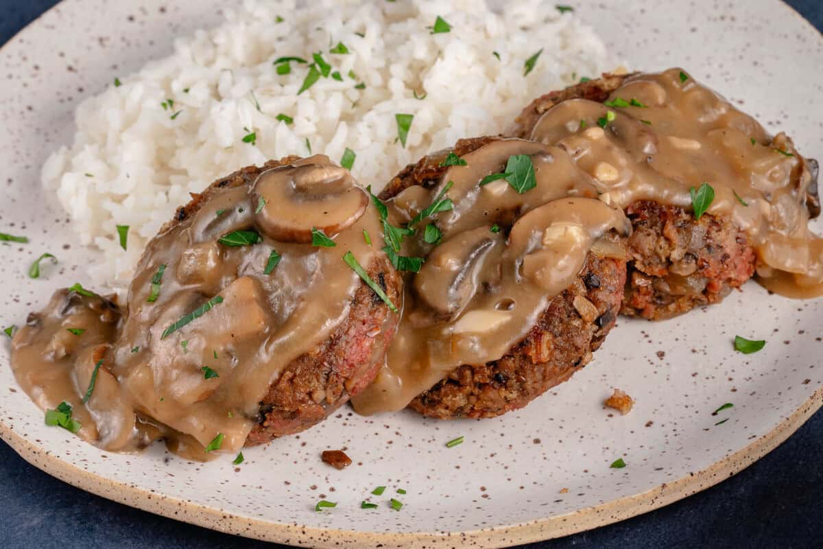 vegan filipino burger steak on a plate topped with mushroom gravy and served with rice