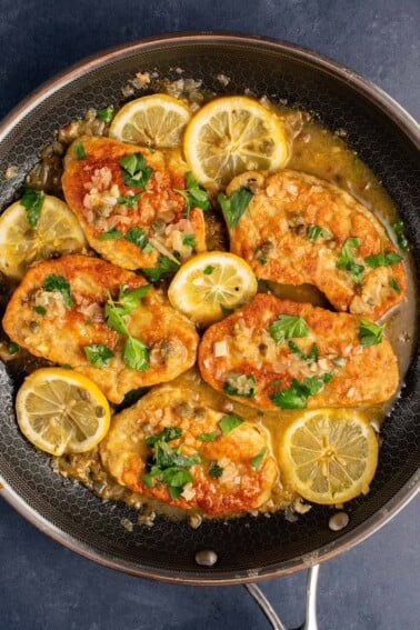 vegan chicken piccata with seitan in a pan topped with fresh herbs and lemon slices