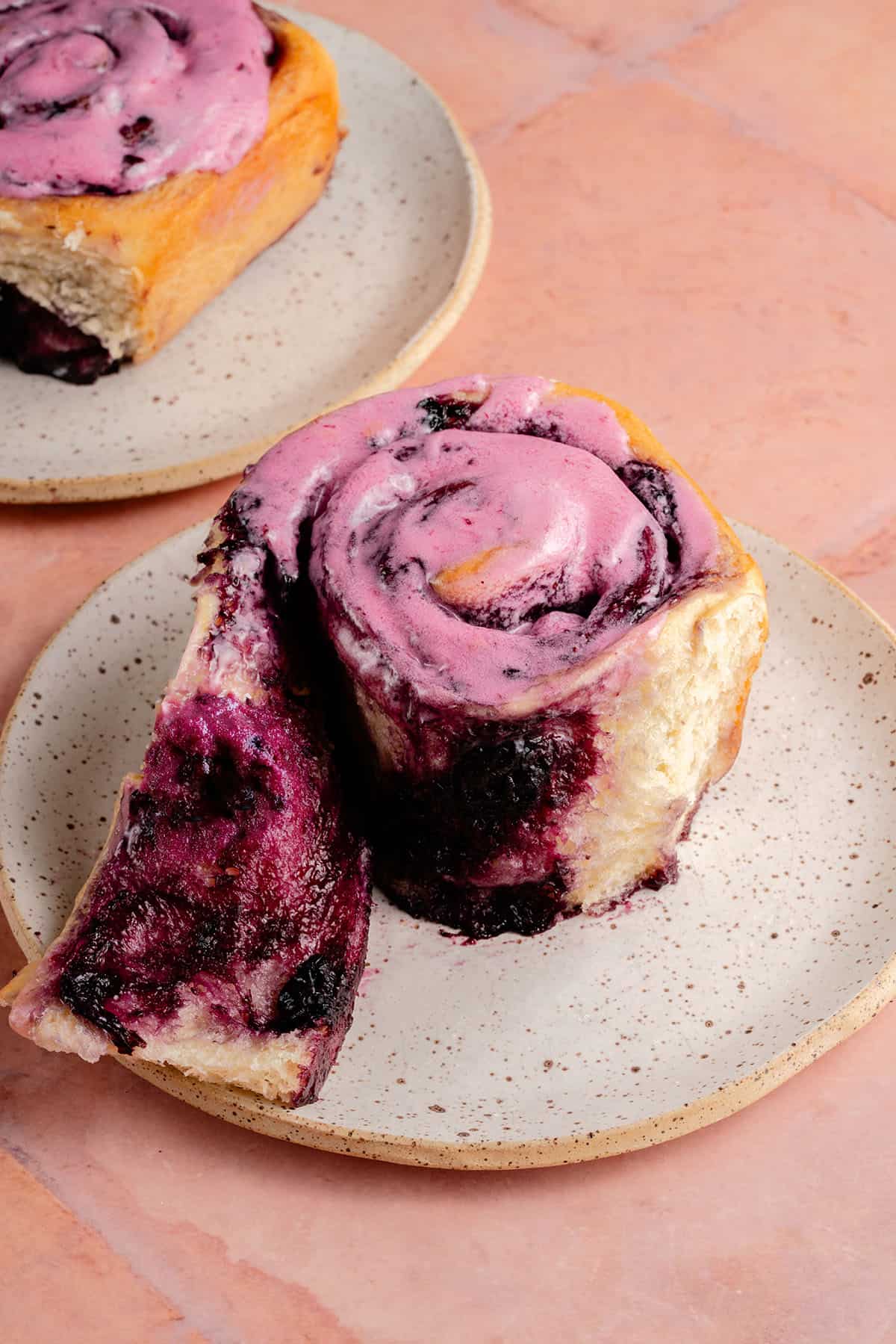 unravelling lemon blueberry roll with blueberry cream cheese frosting on white plate