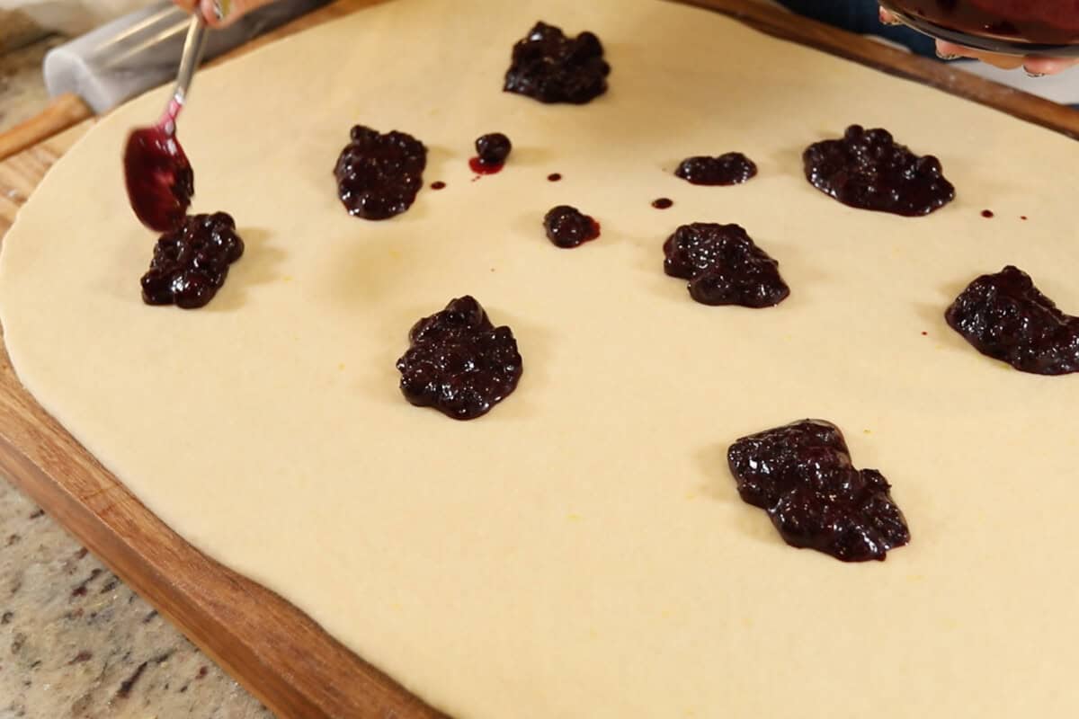 spreading blueberry filling into dough for Vegan Lemon Blueberry Sweet Rolls