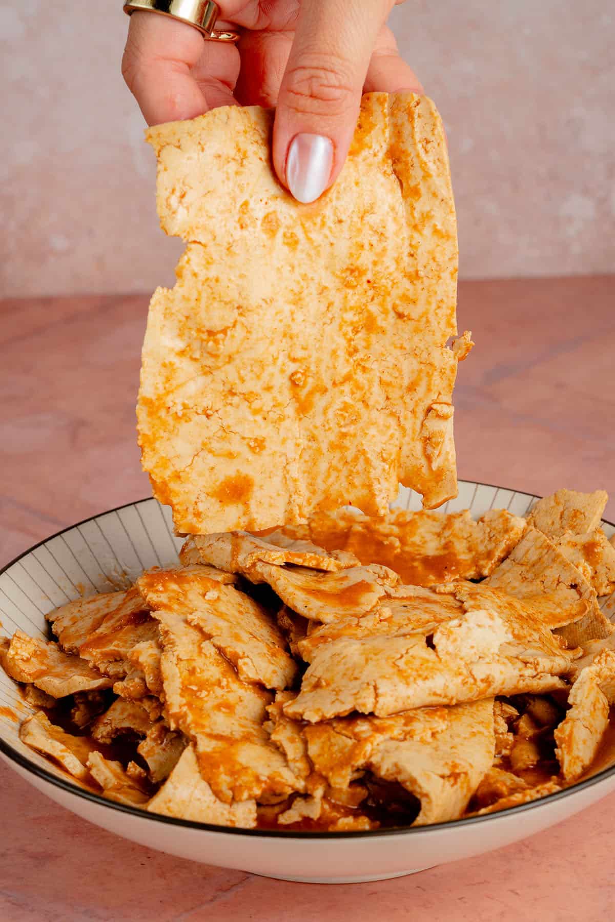 hand holding ham-Style Tofu Deli Meat Slices over bowl
