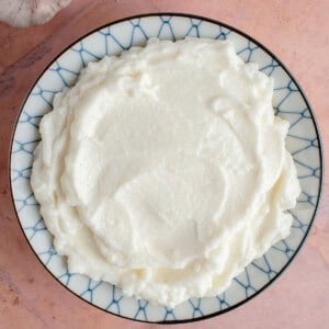 blue and white bowl of fresh Lebanese Garlic Sauce (Toum) on pink backdrop