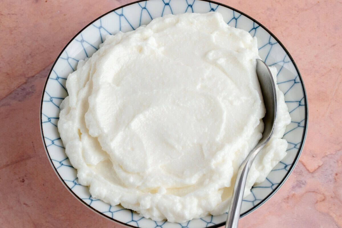 horizontal photo of blue and white bowl of fresh Lebanese Garlic Sauce (Toum) with spoon on pink backdrop