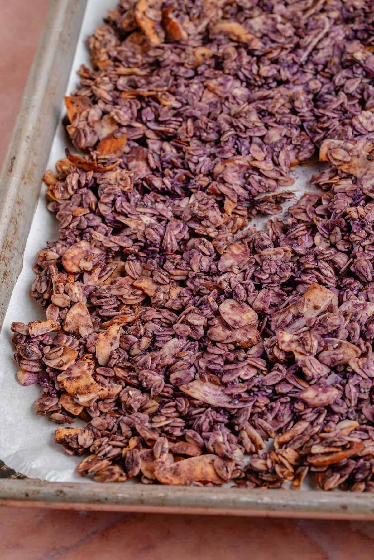 toasted Ube Coconut Granola on baking sheet against pink backdrop